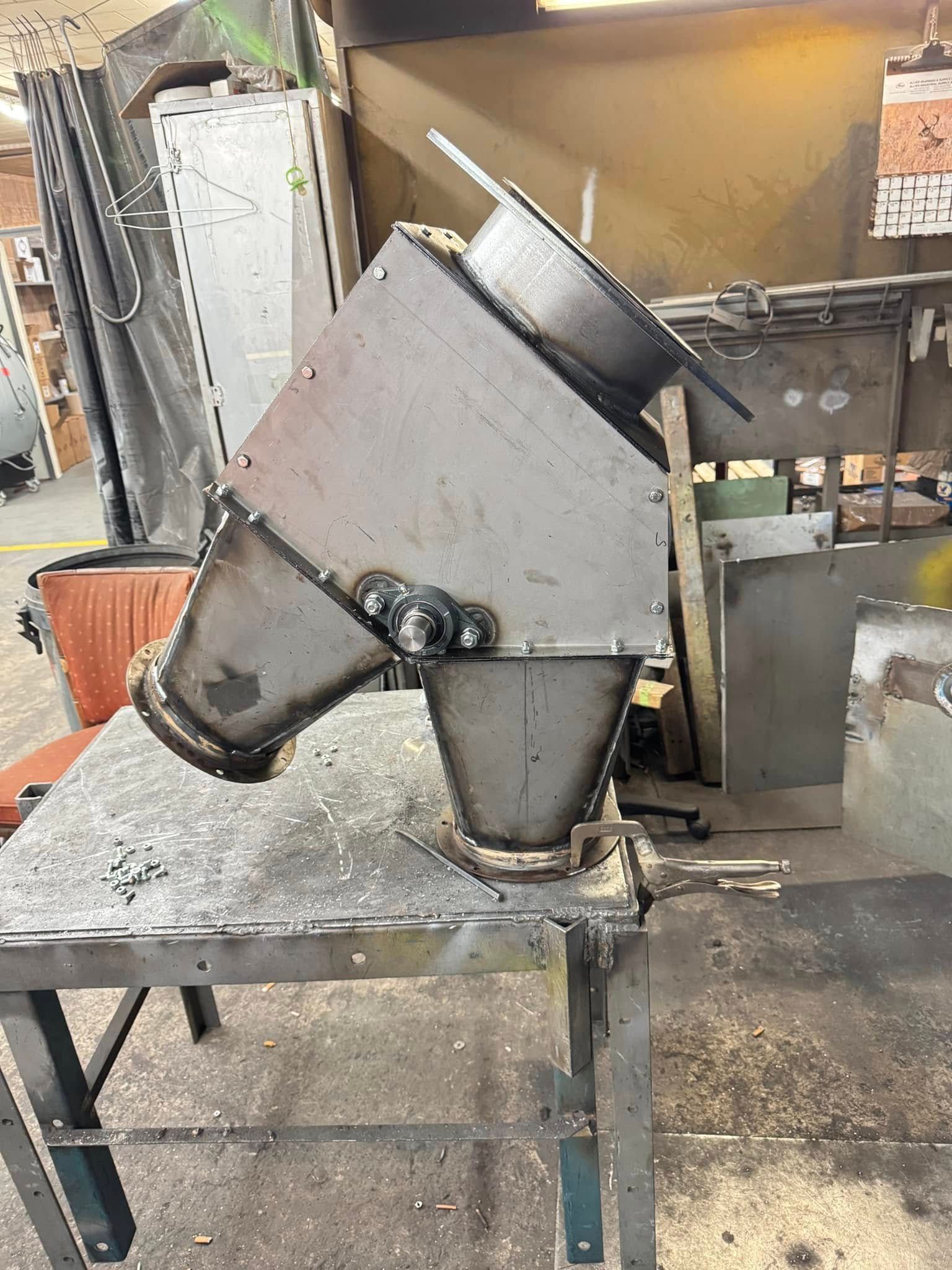 Metal hopper, welded construction, angled on a work table in a workshop.