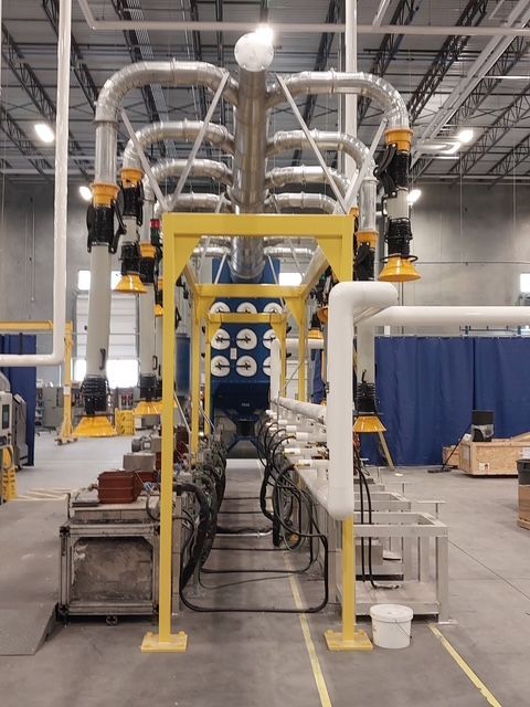 Yellow industrial metal structure with pipes and hoses in a factory setting.