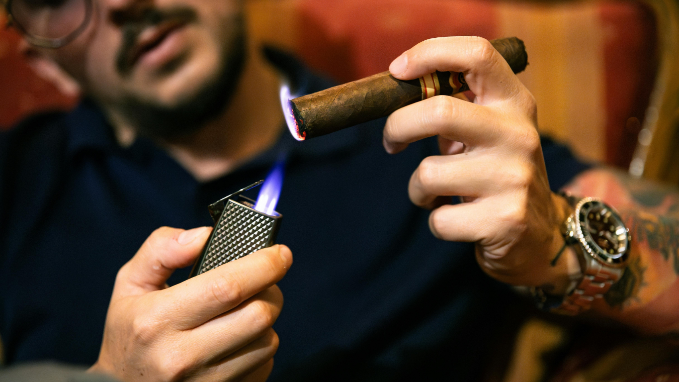 Person lighting a cigar with a lighter, close-up in a warm indoor setting.