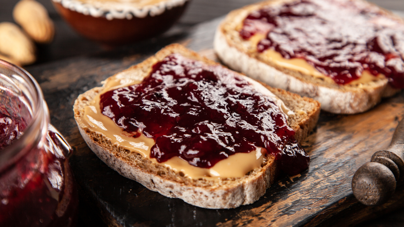 Slices of bread topped with peanut butter and red jam on a rustic wooden board