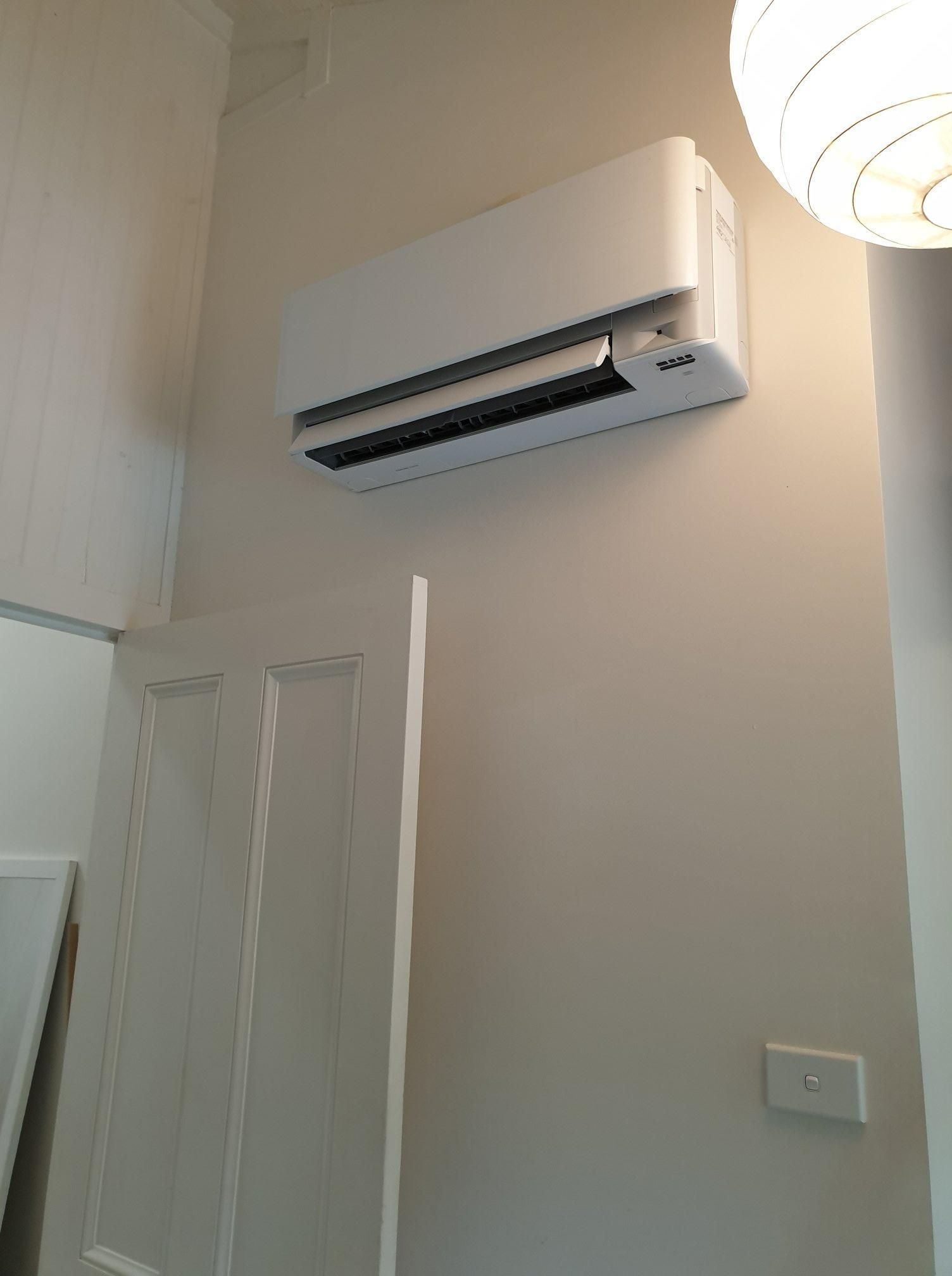 A White Air Conditioner Is Mounted On A Wall Next To A Door — Jervis Bay Airconditioning In Huskisson, NSW