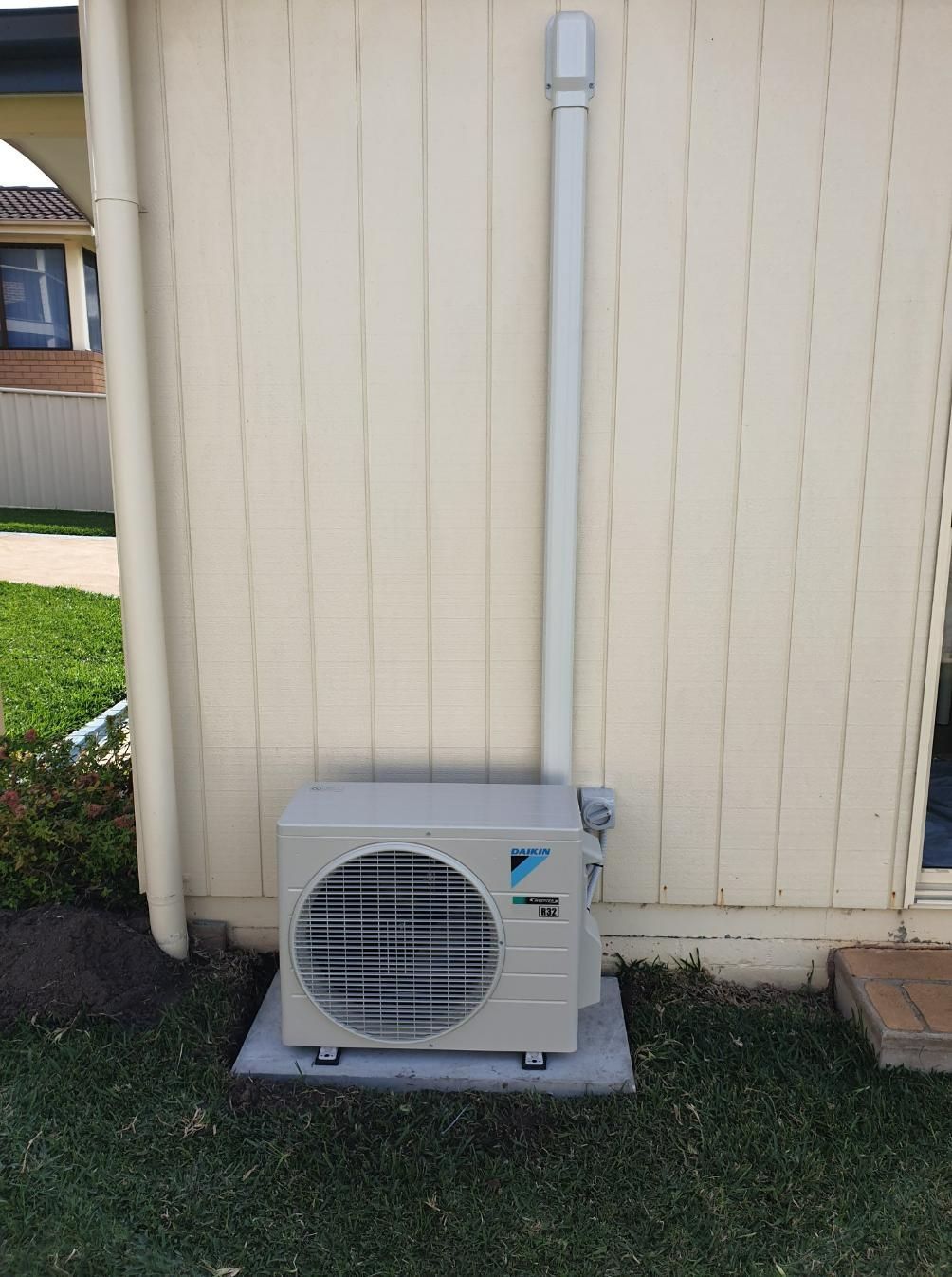 A White Air Conditioner Is Mounted On The Side Of A House — Jervis Bay Airconditioning In Huskisson, NSW