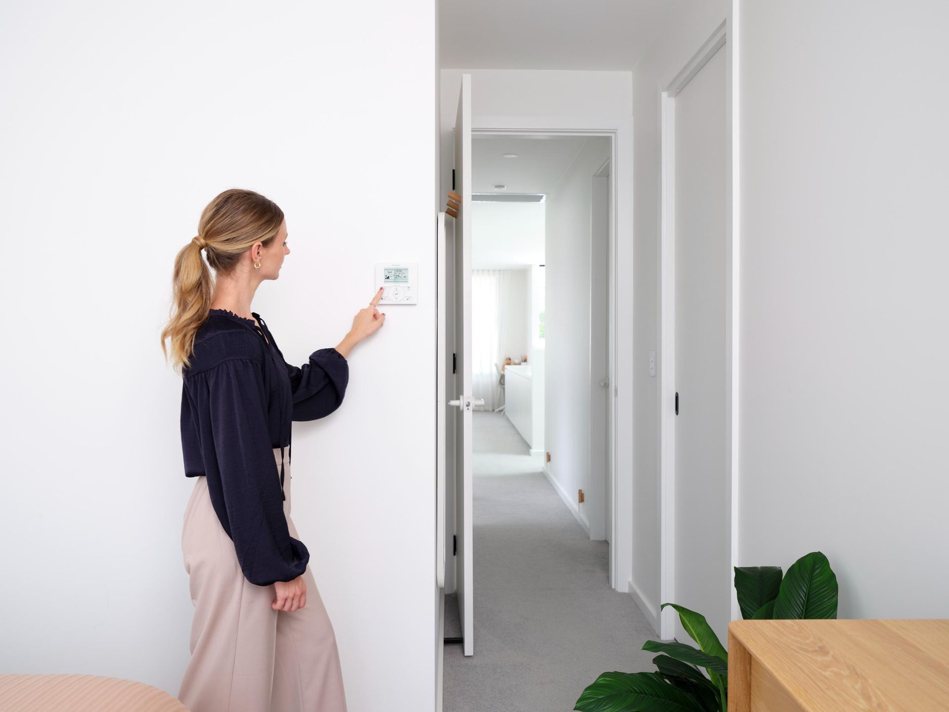 A Woman Is Standing In A Hallway Adjusting A Thermostat — Jervis Bay Airconditioning In Ulladulla, NSW