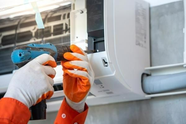 A Person Is Fixing An Air Conditioner With A Drill — Jervis Bay Airconditioning In Kiama, NSW