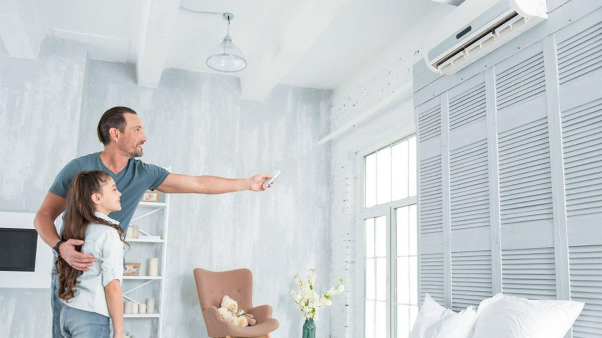 A Man And A Girl Are Standing In A Living Room Looking At An Air Conditioner — Jervis Bay Airconditioning In Ulladulla, NSW