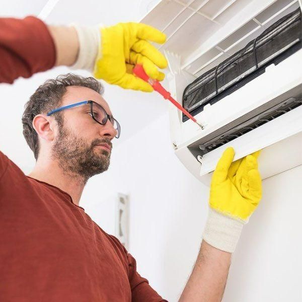 A Man Wearing Yellow Gloves Is Fixing An Air Conditioner With A Screwdriver — Jervis Bay Airconditioning In Ulladulla, NSW