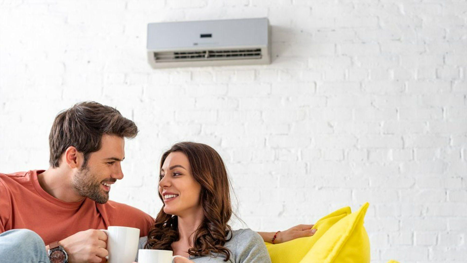 A Man And A Woman Are Sitting On A Bean Bag Chair Drinking Coffee — Jervis Bay Airconditioning In Berry, NSW