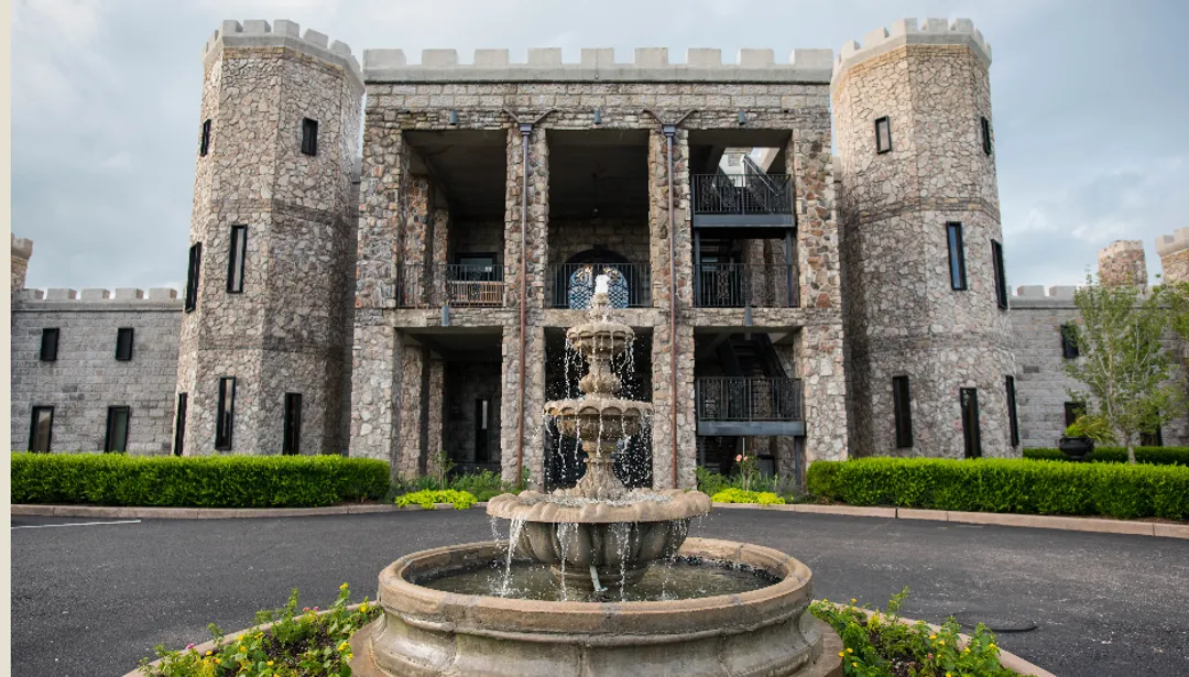 Stone castle facade with a fountain in front.