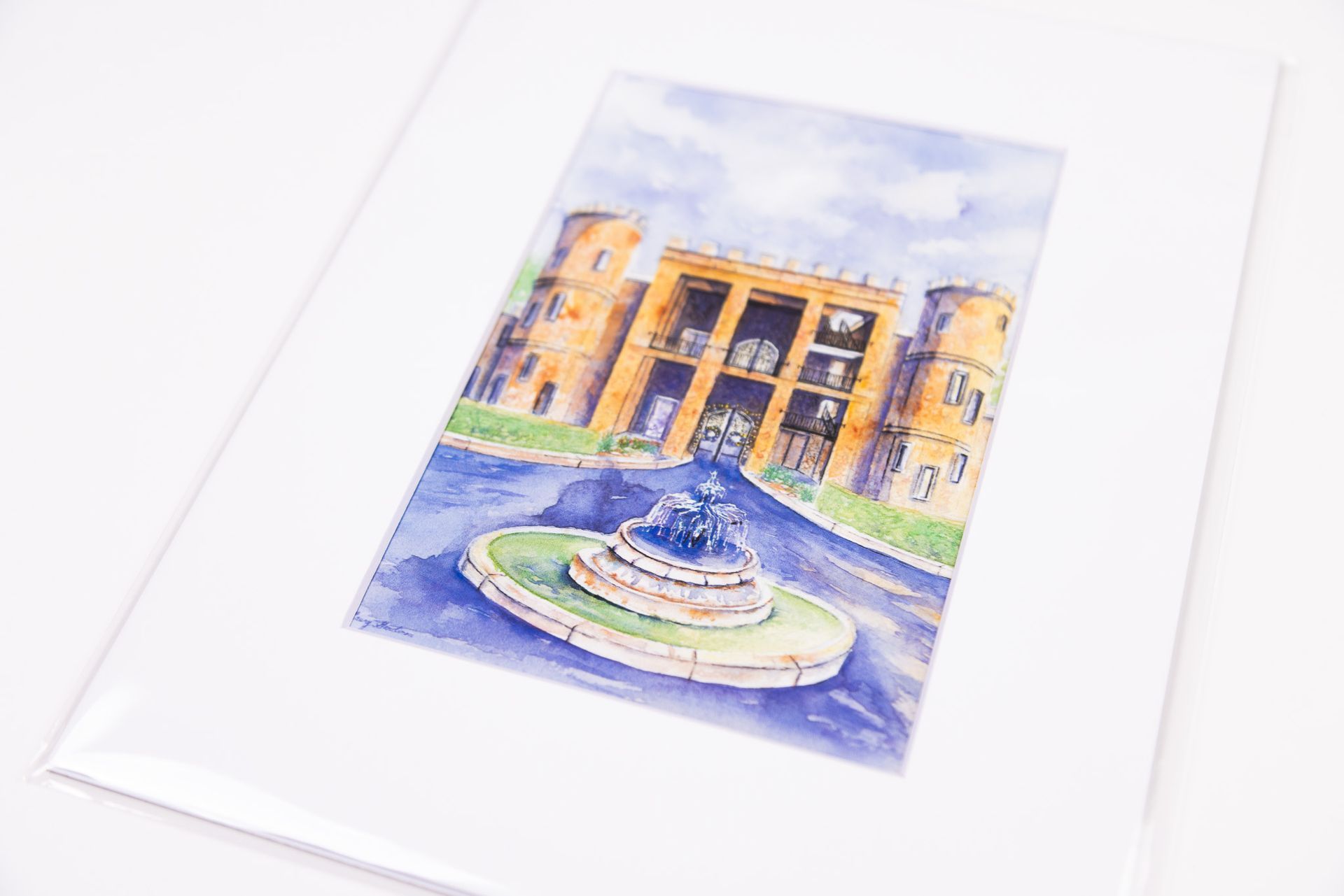 Watercolor painting of a building with round towers, fountain in front, sky overhead.