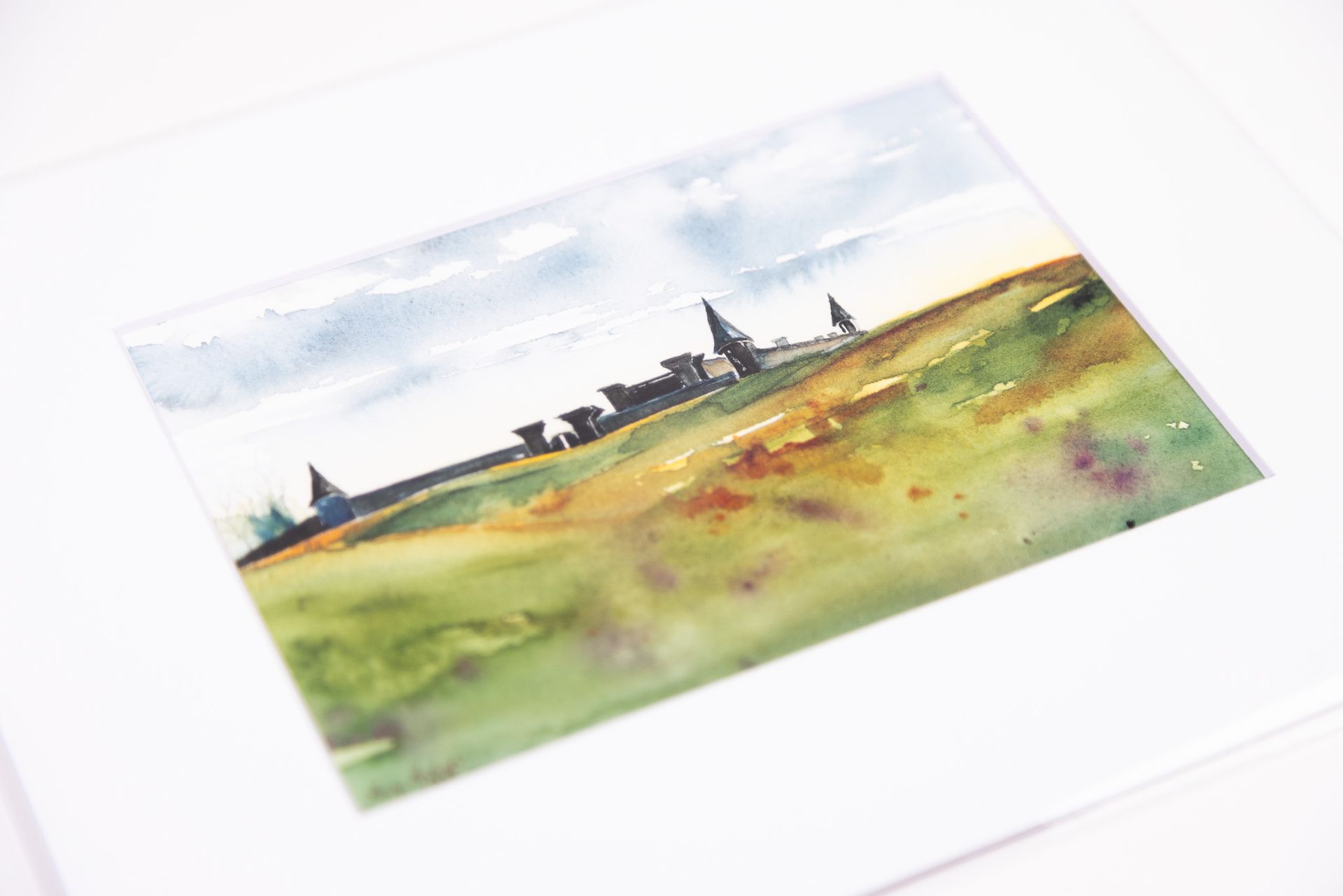 Watercolor landscape painting with a field and distant buildings.