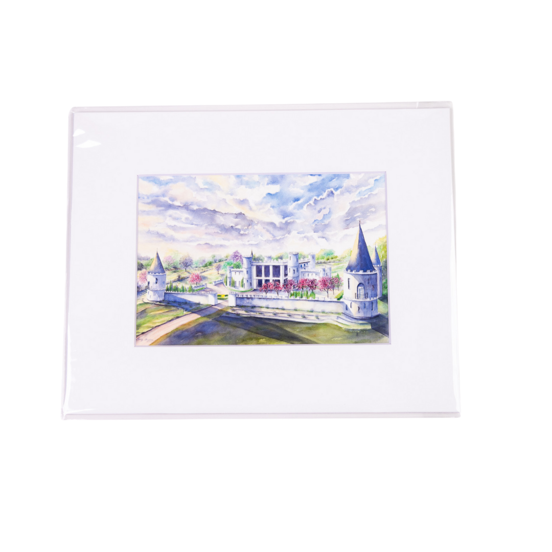 Watercolor painting of a white castle with towers, trees, and blue sky, mounted in a white mat.