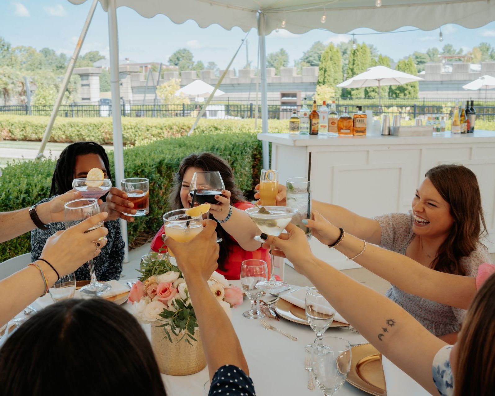 Group of women toasting with drinks outdoors under a tent.