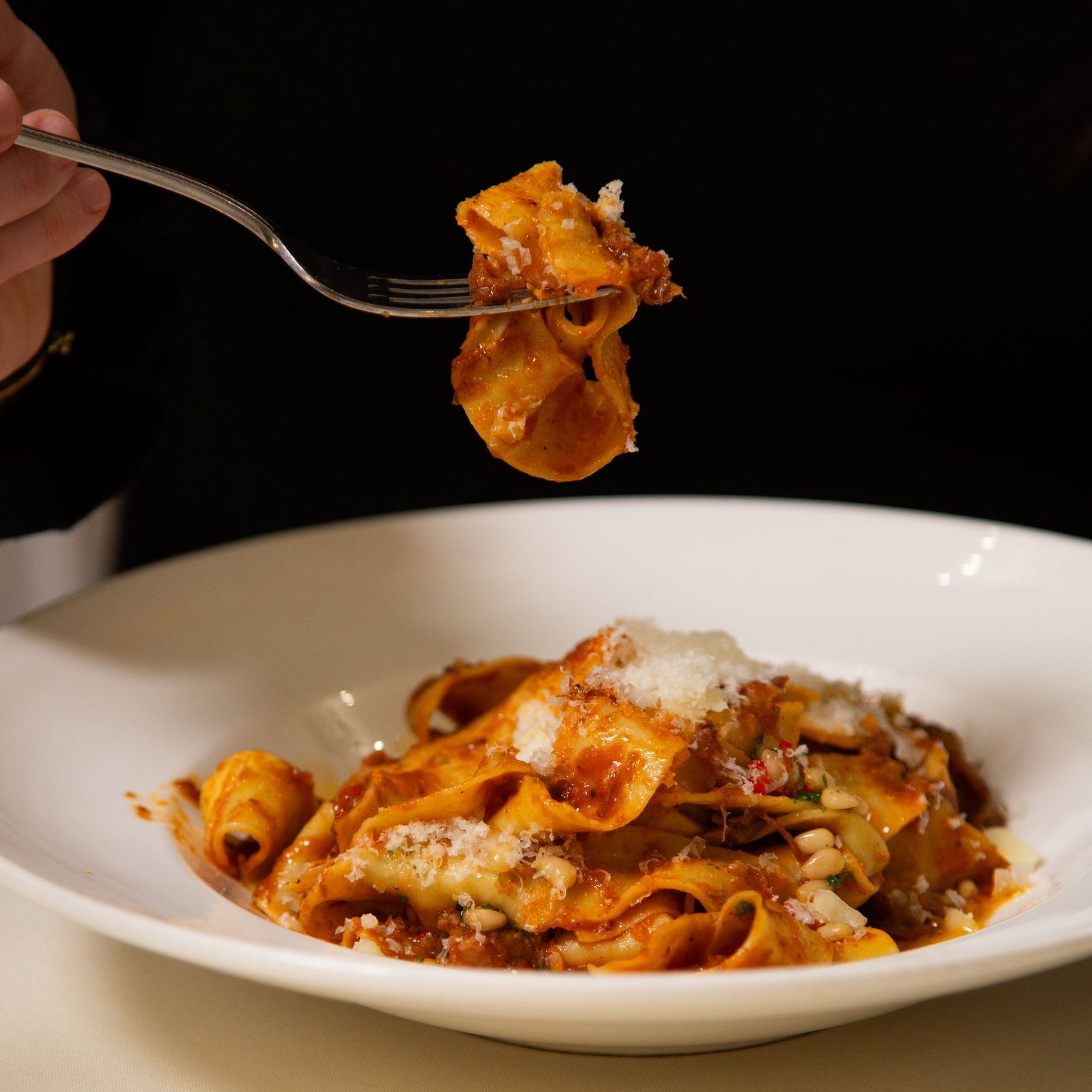 Forkful of pappardelle pasta with meat sauce, being lifted from a white bowl.