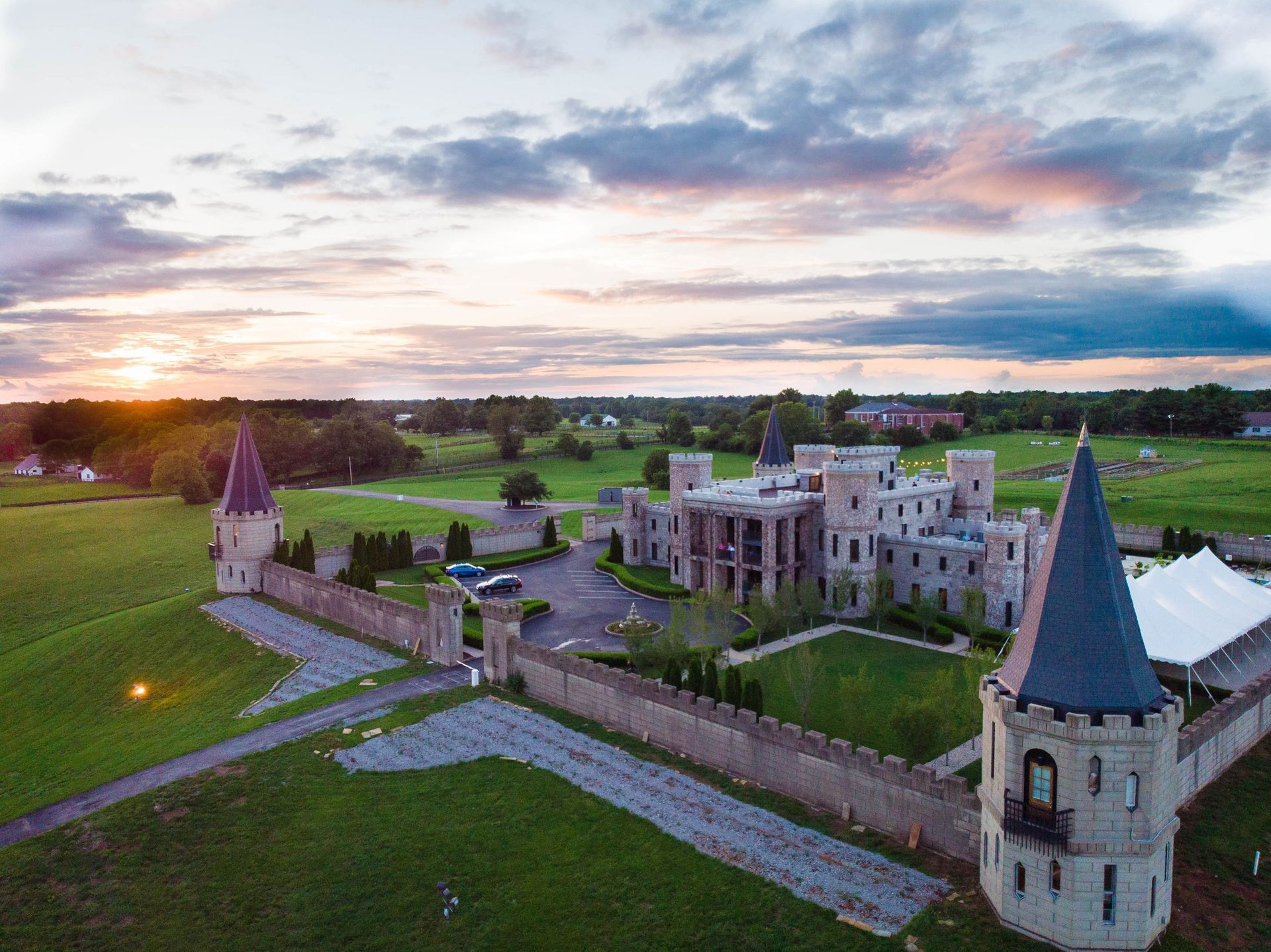Castle at sunset, stone walls and towers, green lawns, car park.