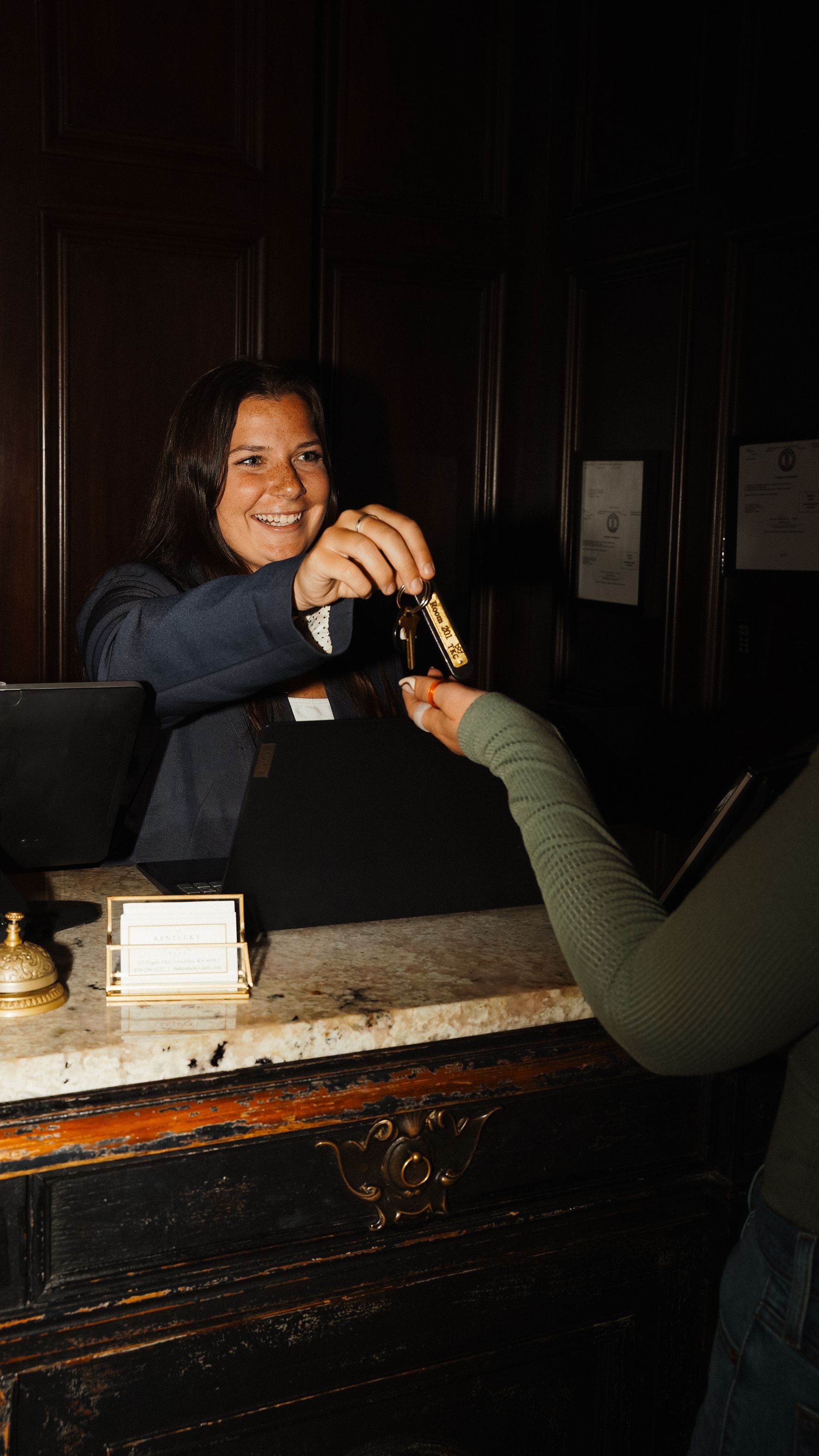 A smiling hotel concierge handing a customer keys to a hotel room over the front desk