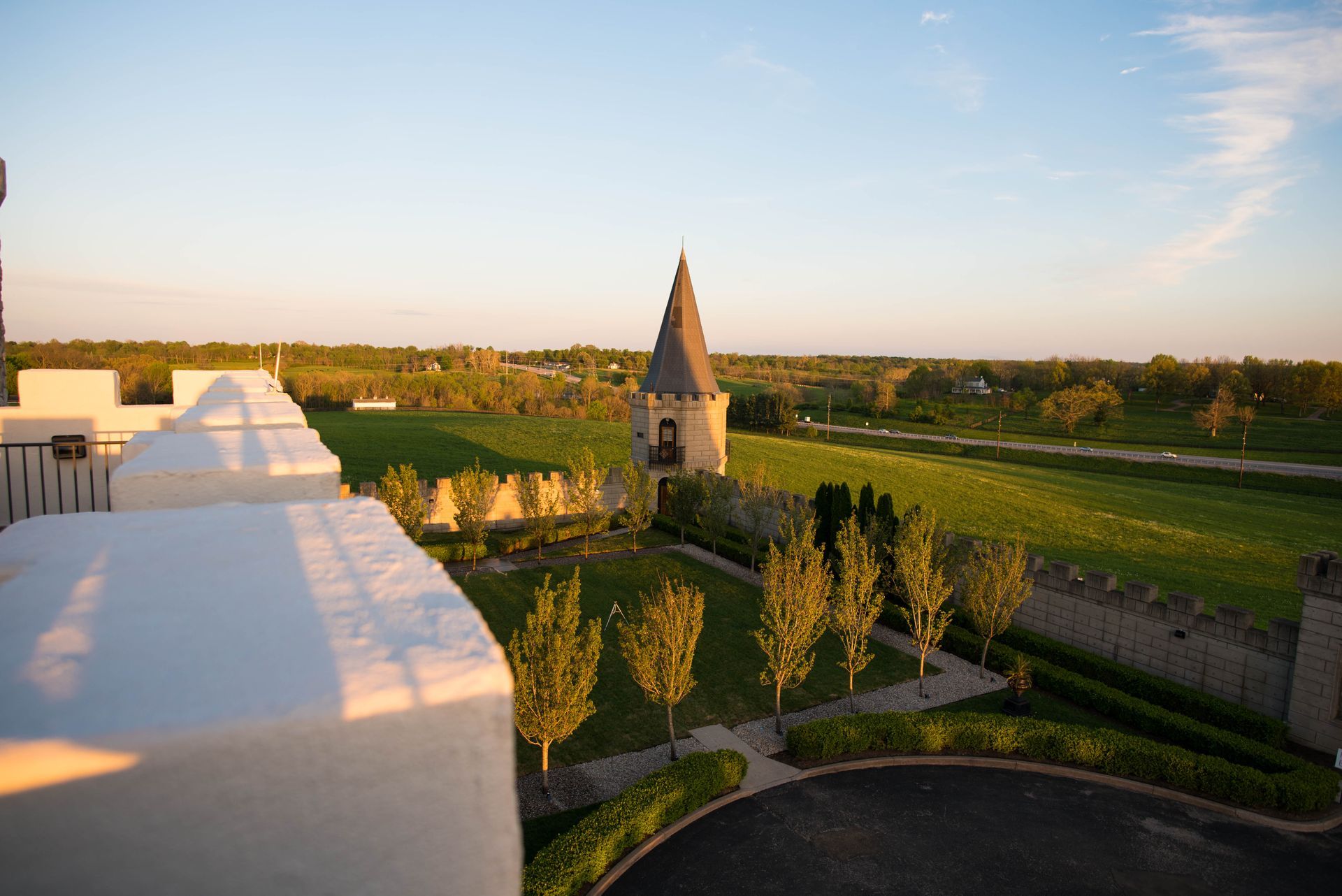 Exterior shot of castle-like building with tower and green fields during sunset.