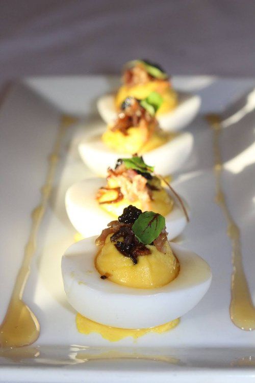 Deviled eggs, topped with bacon and greens, drizzled with sauce on a white rectangular plate.