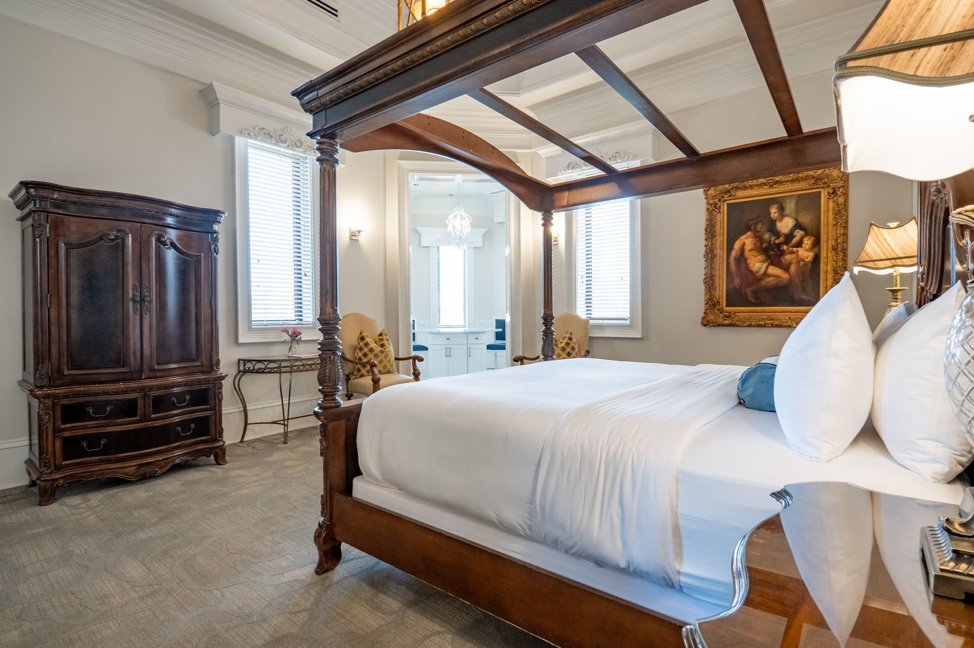 Elegant bedroom with a dark wood canopy bed, ornate wardrobe, and a painting.