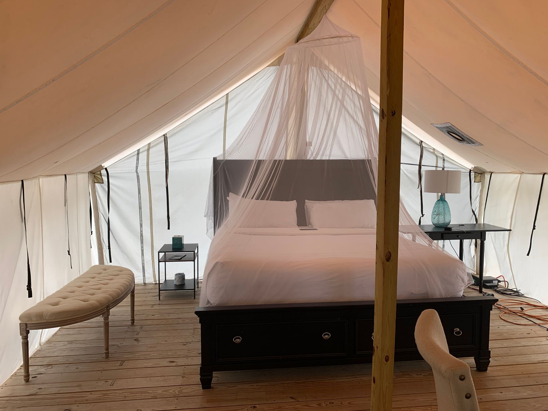 Interior of a glamping tent with a bed, bench, side table, and a decorative canopy.