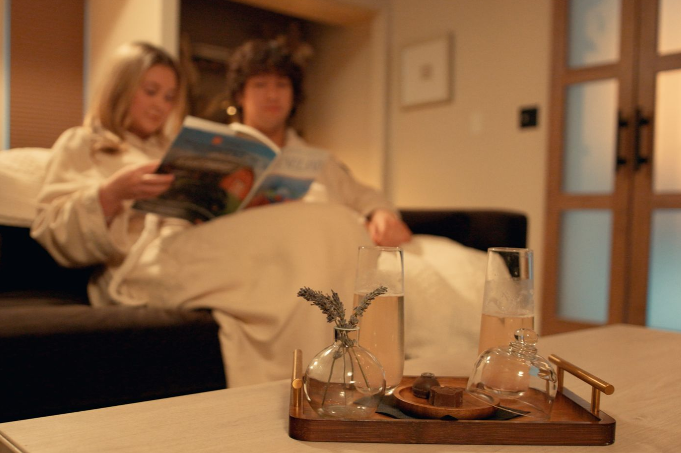 A man and woman sitting on a couch in a spa, wearing spa robes and looking through a travel magazine