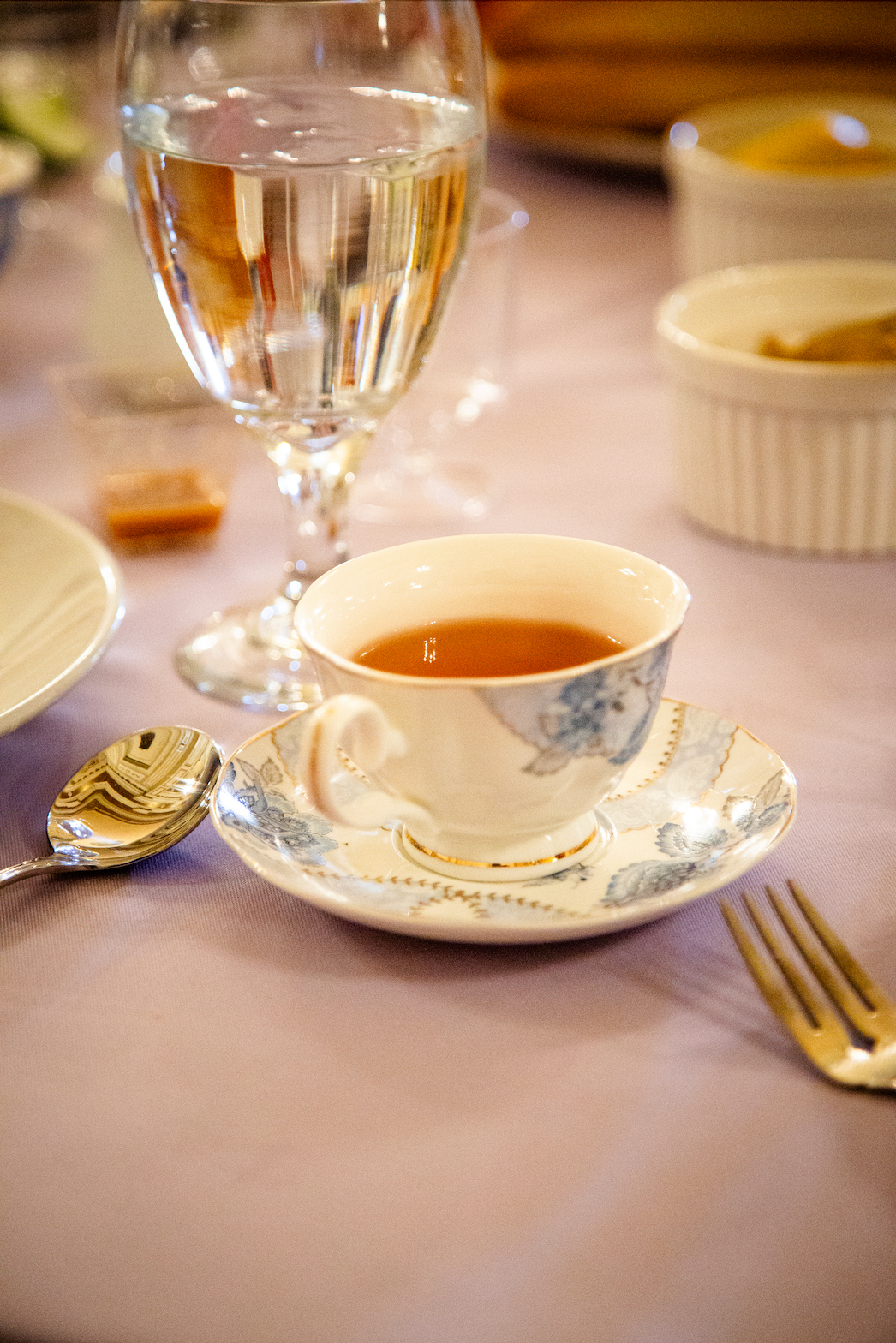 A teacup with tea on a saucer, a water glass, and silverware on a purple tablecloth.