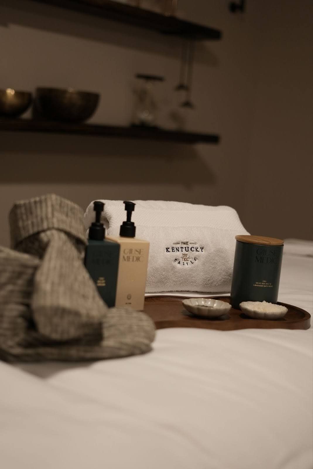 Spa setting with toiletries on a tray, towels, and shelves in the background.