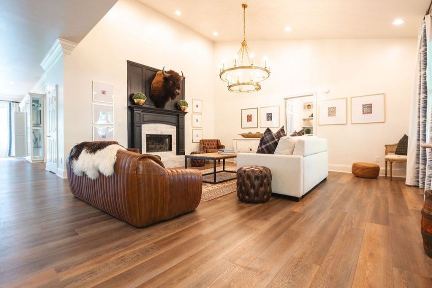 Spacious living room with leather furniture, fireplace, chandelier, and hardwood floors.