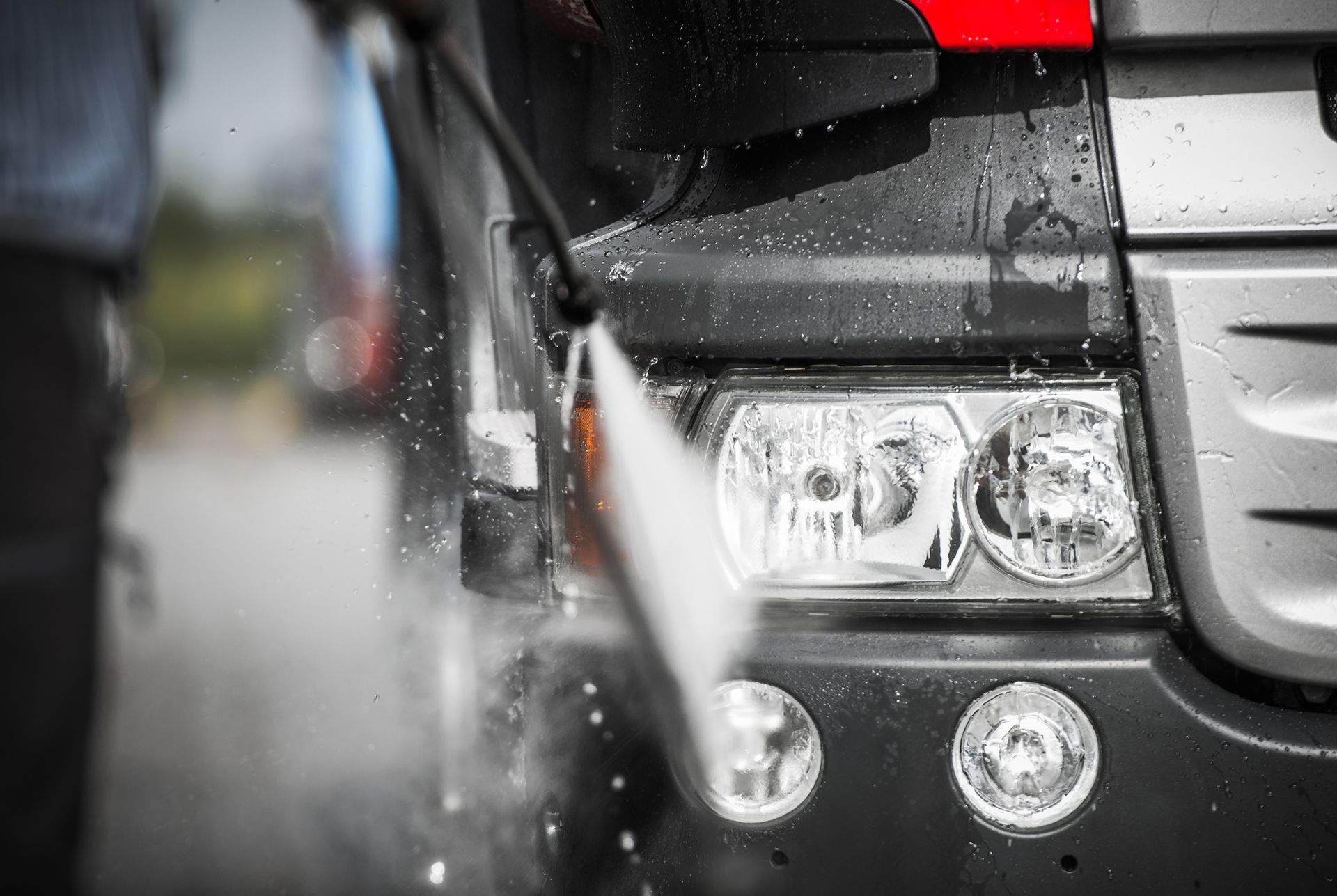 Truck headlight being power washed, with water spraying.