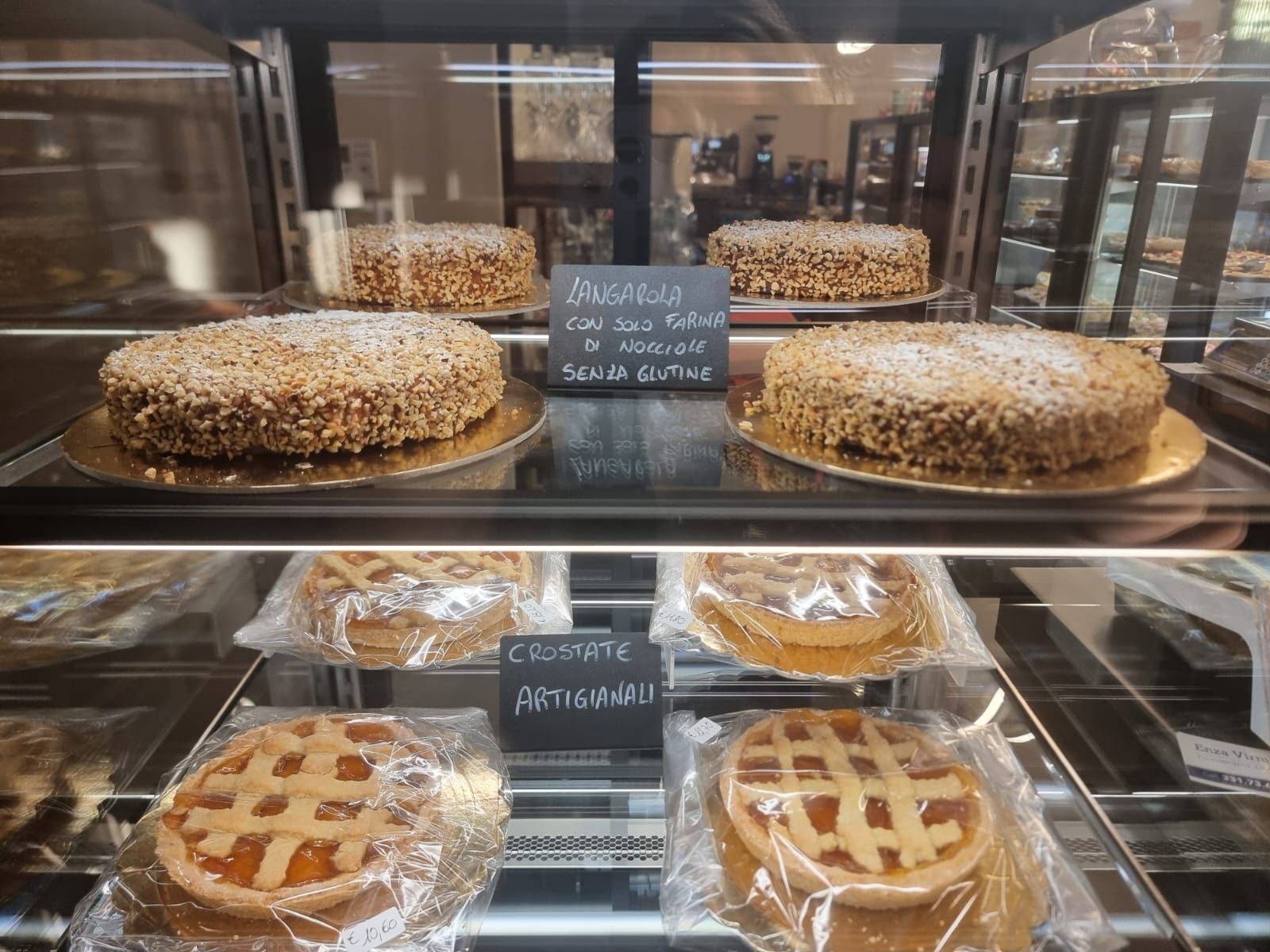Torte e crostate in una vetrina di vetro, con cartelli scritti a mano.
