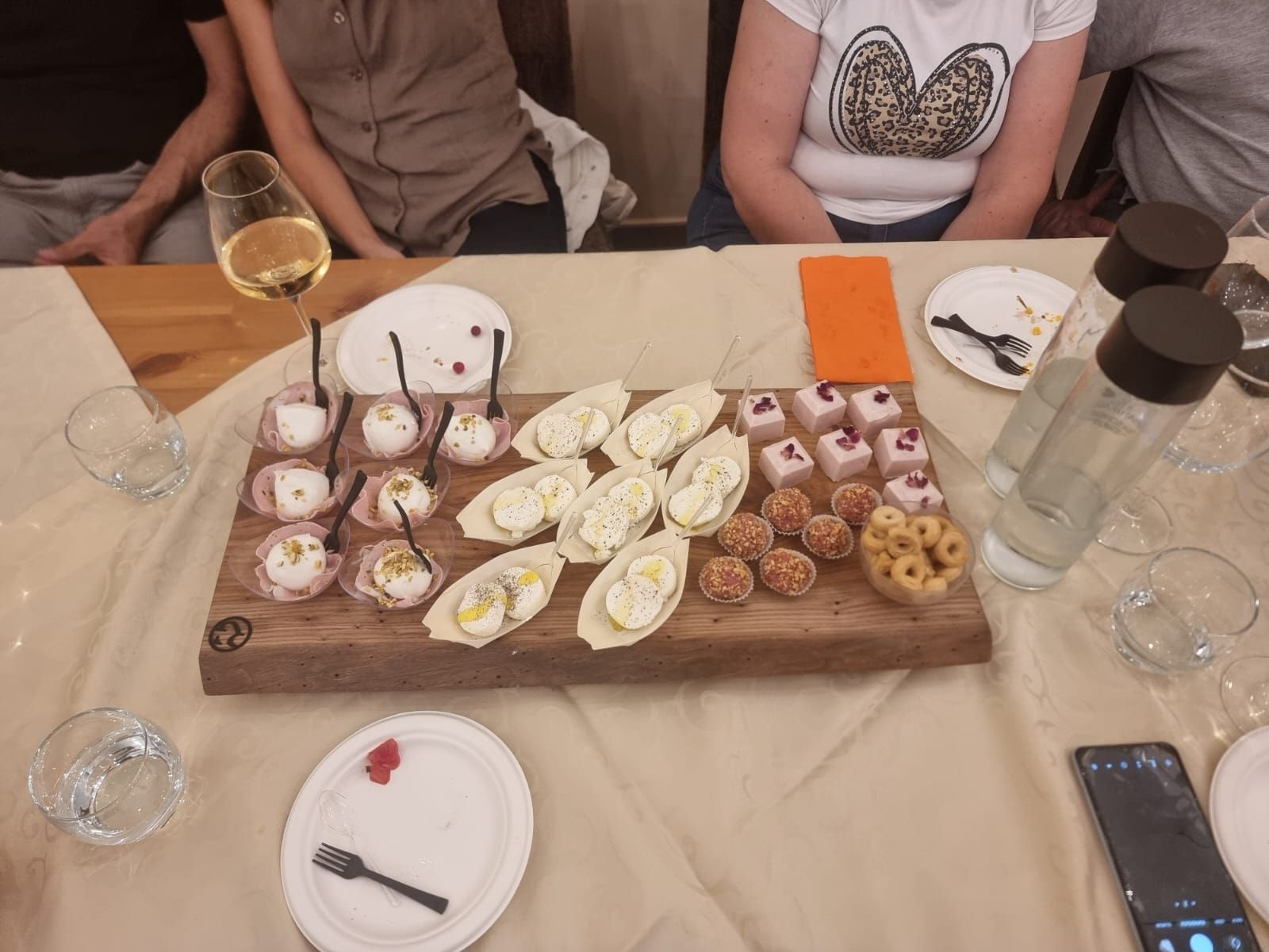 Un vassoio di legno con antipasti assortiti su un tavolo con persone sullo sfondo.