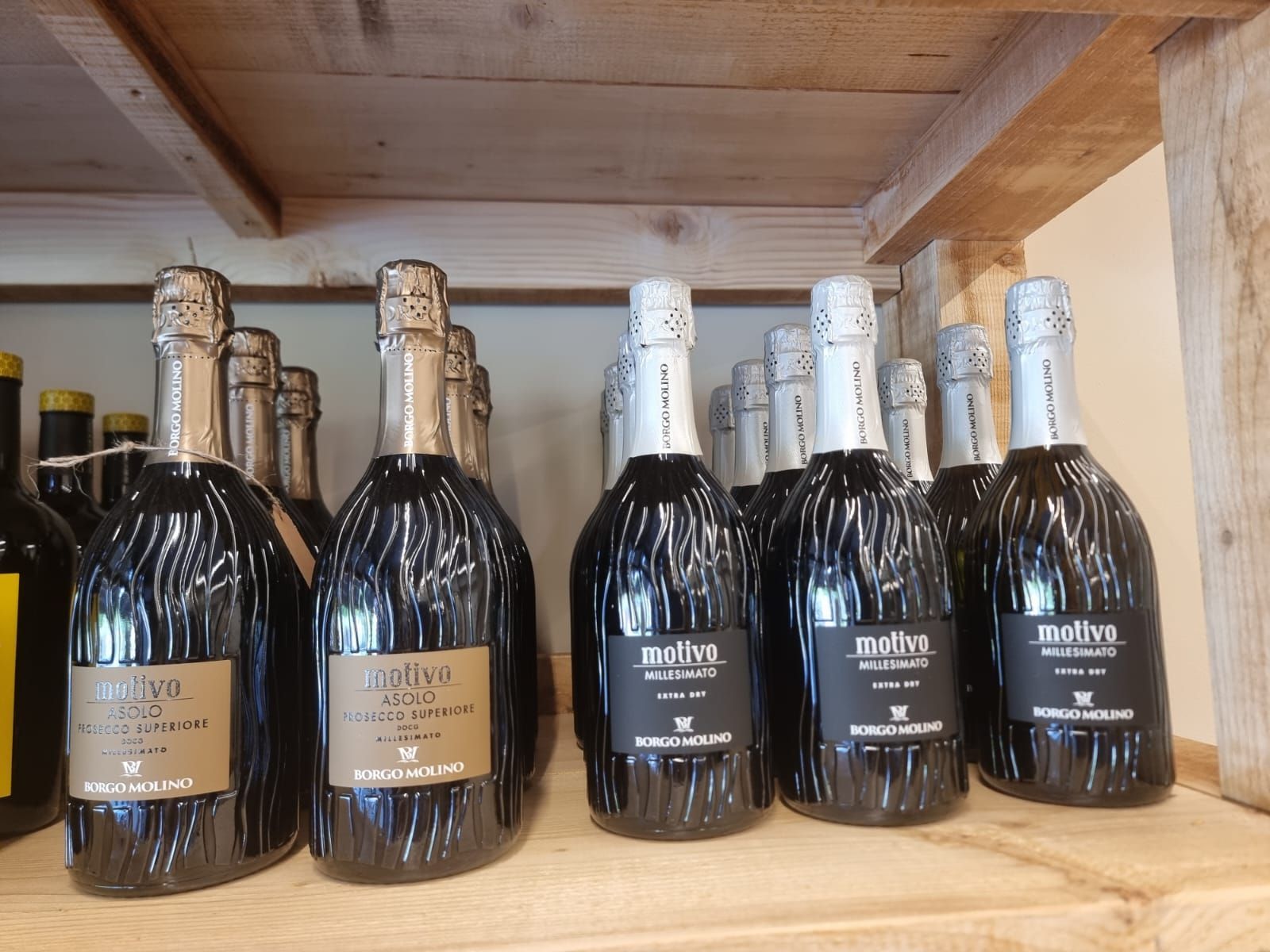 Bottiglie di spumante su uno scaffale di legno, in un ambiente da negozio.