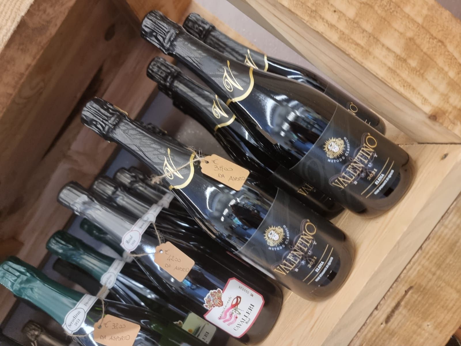 Bottiglie di spumante, per lo più con etichette nere, in casse di legno. Alcune hanno l'etichetta.
