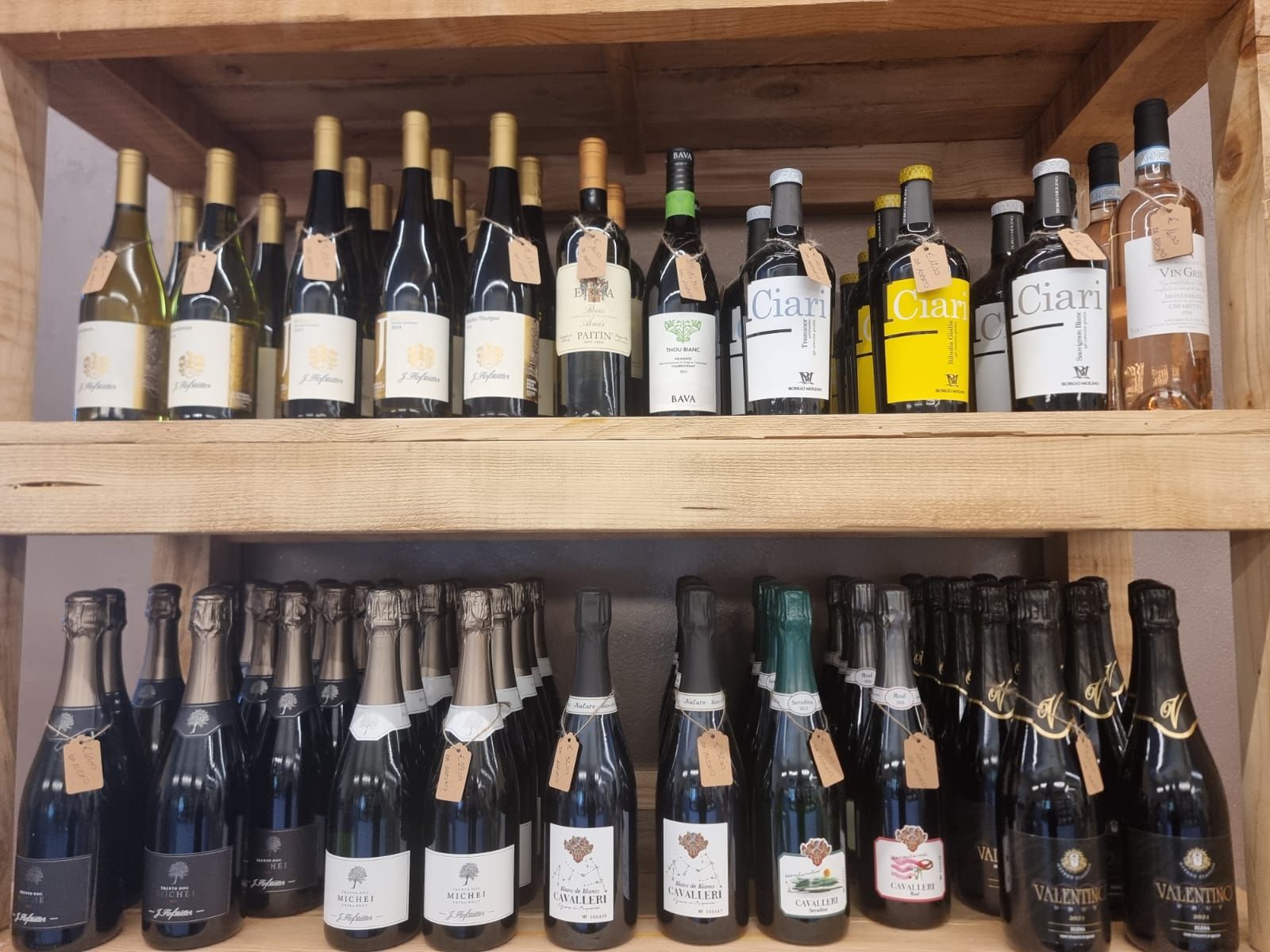 Bottiglie di vino su scaffali di legno in un negozio, con bottiglie bianche e scure.