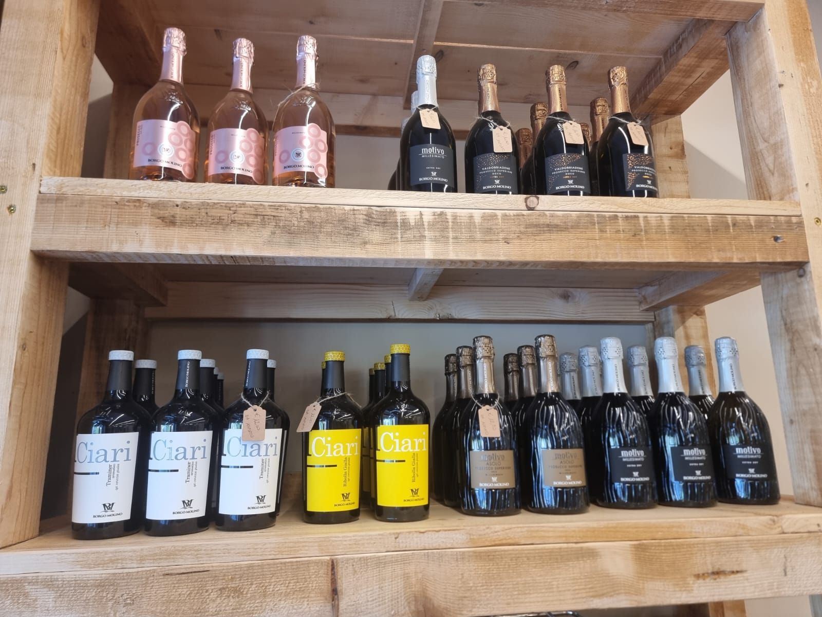 Scaffali in legno pieni di bottiglie di vino di vario tipo, tra cui spumanti e vini fermi.