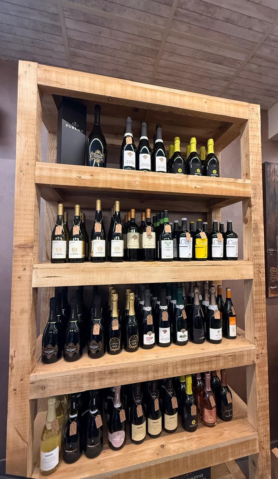 Scaffale di legno pieno di varie bottiglie di vino, esposto in un negozio.