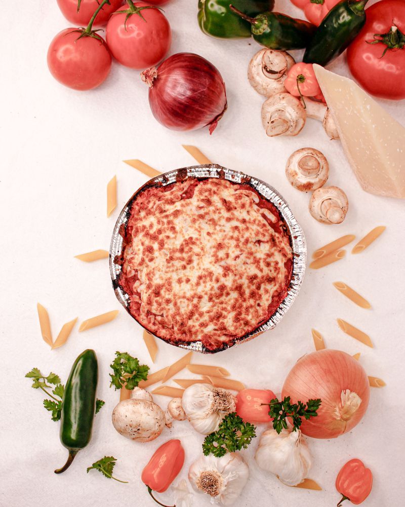 A pizza surrounded by vegetables and pasta on a table