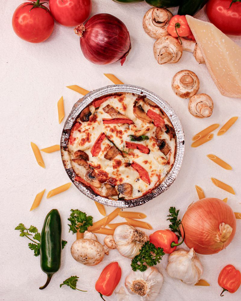 A pizza is surrounded by vegetables and pasta on a table.
