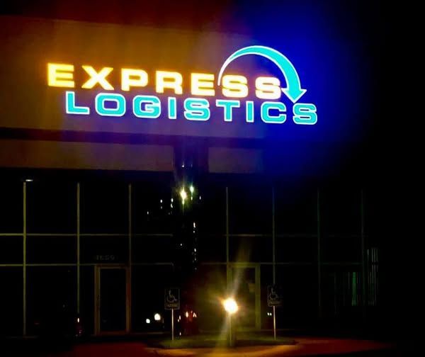 Neon sign reading “EXPRESS LOGISTICS” glowing blue and orange on a dark building facade at night