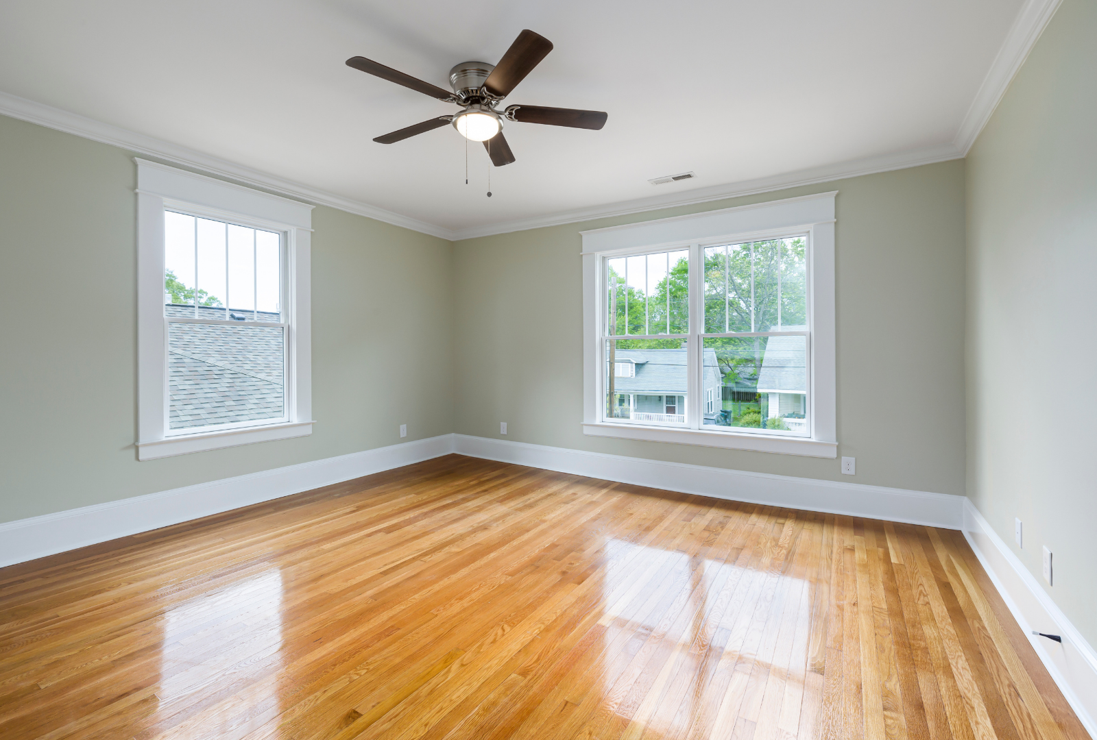 Empty living room with hardwood floors, gray walls, two windows, and a ceiling fan.