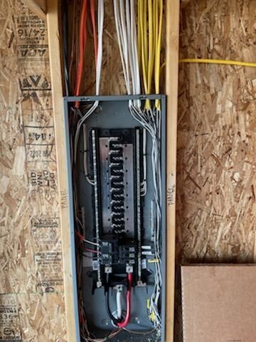 Electrical panel with wires and components mounted in a wall stud cavity during construction.