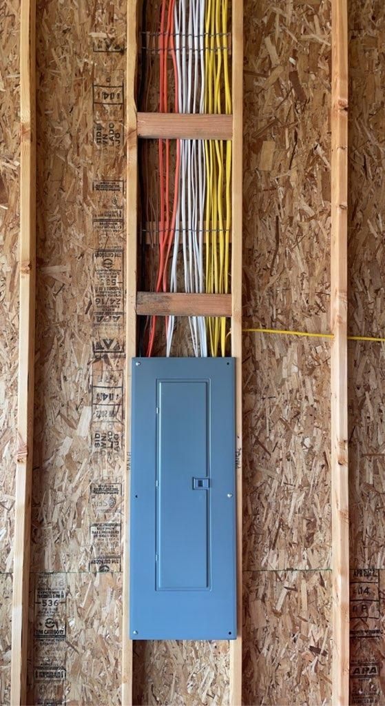 Blue electrical panel mounted on a rough unfinished wall with exposed wiring and insulation