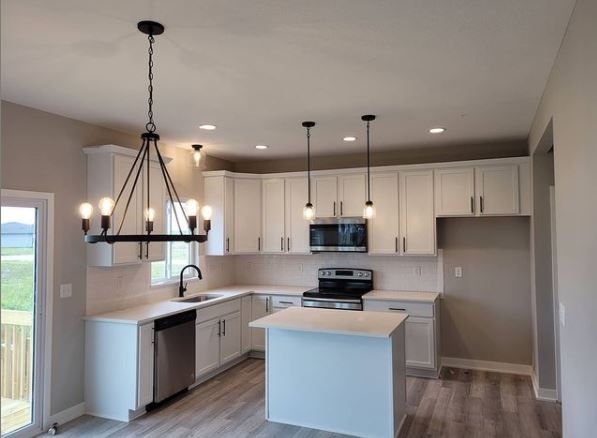 Modern white kitchen with island, stainless appliances, pendant lights, and wood-look flooring