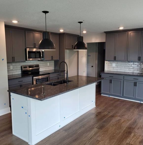 Modern kitchen with dark cabinets, white island, stainless appliances, and wood flooring