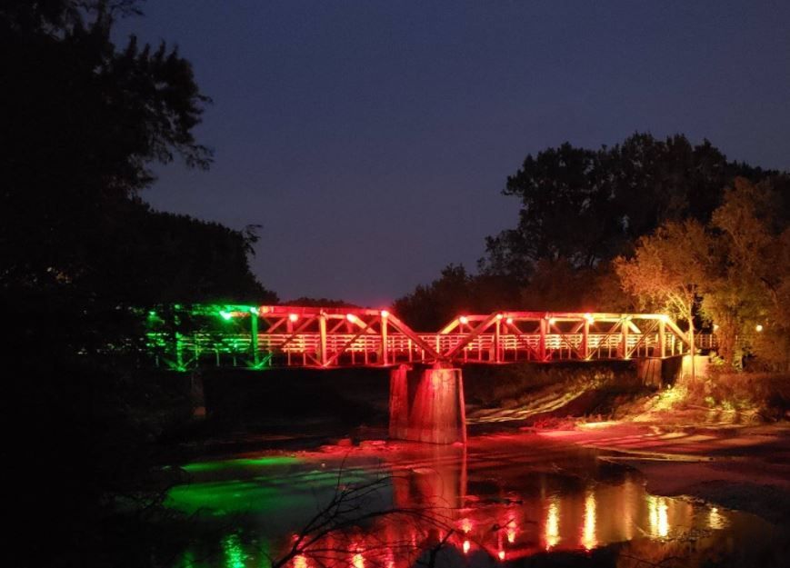 Colorfully lit bridge glowing red, green, and orange at night, reflected in water