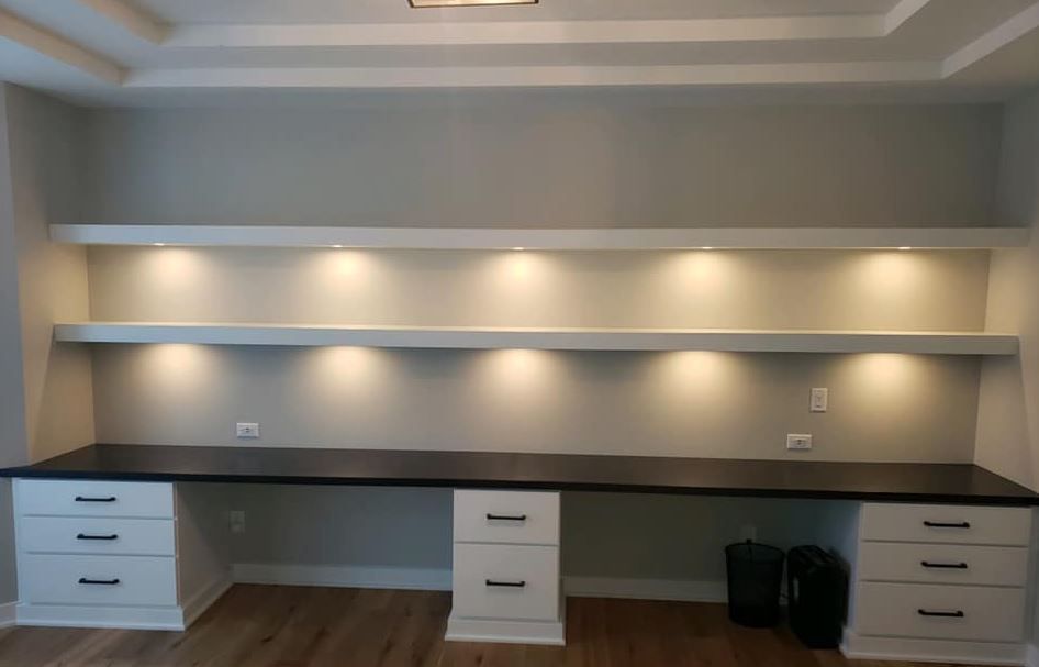 Built-in office desk nook with white drawers, dark countertop, and recessed wall lighting