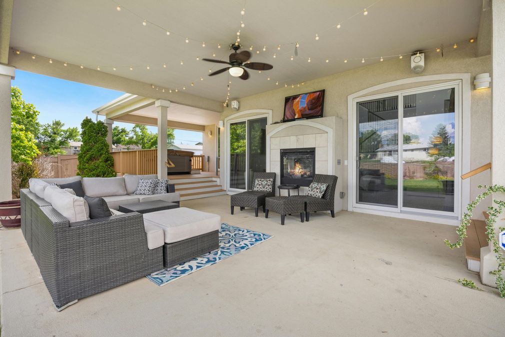 Covered patio with wicker sectional, fire pit table, and sliding glass doors overlooking a backyard
