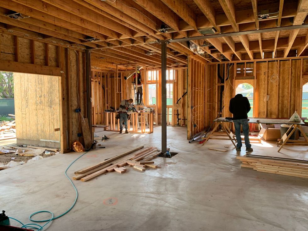 Interior of a wood-framed house under construction, with workers, tools, and exposed beams.