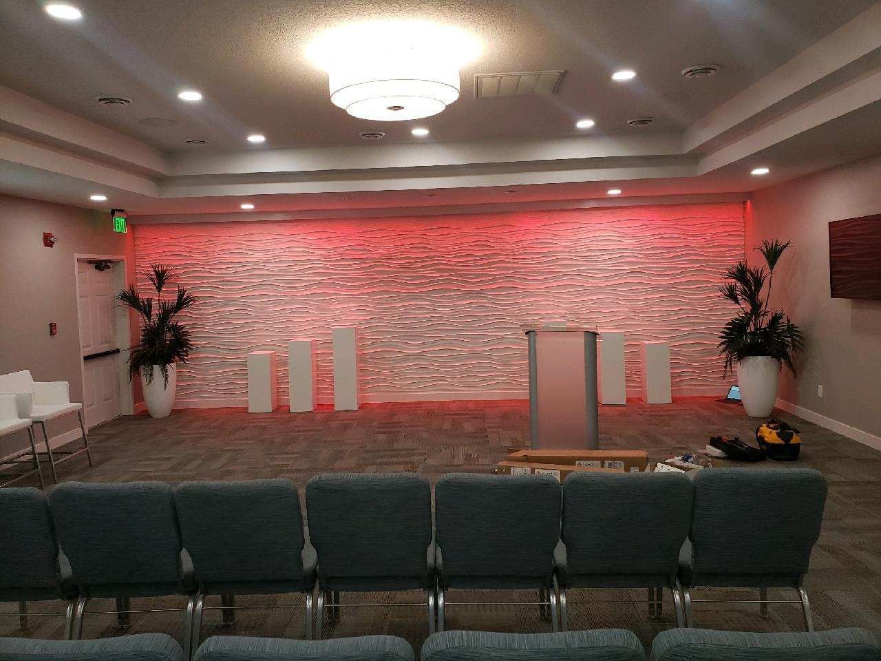 Empty conference room with rows of chairs, a stage, and red-lit brick wall backdrop
