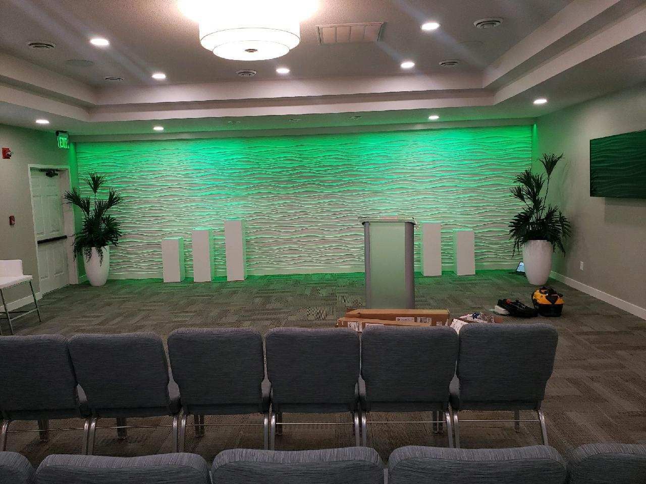 Empty stage with green uplighting, podium, and rows of chairs in a small conference room