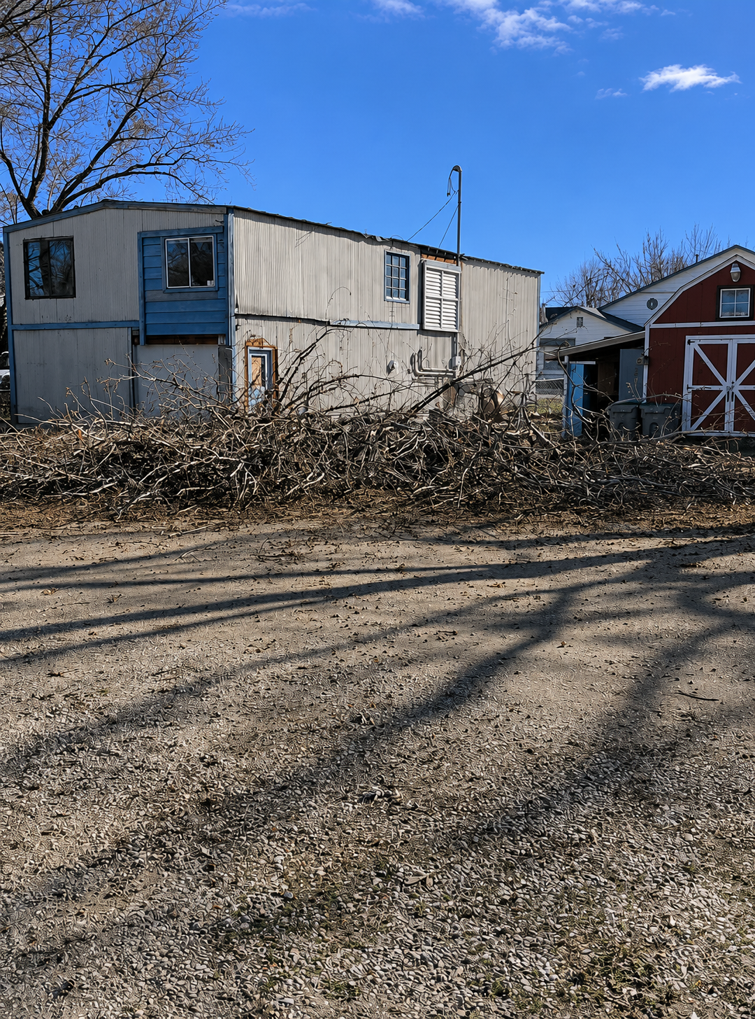 Mobile home beside leaf piles and a red barn on a sunny day